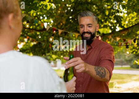 Uomo sorridente che passa una bottiglia di birra Foto Stock