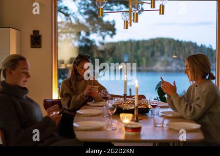 Le donne che si siedono al tavolo da pranzo e usano i telefoni Foto Stock