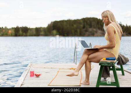 Donna in costume da bagno con computer portatile sul lago Foto Stock