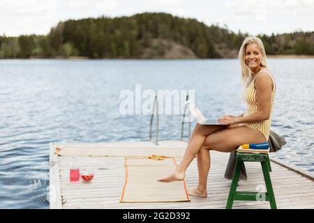 Donna in costume da bagno con computer portatile sul lago Foto Stock