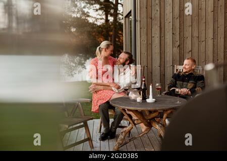 Coppia con un amico seduto sul patio e bere vino Foto Stock