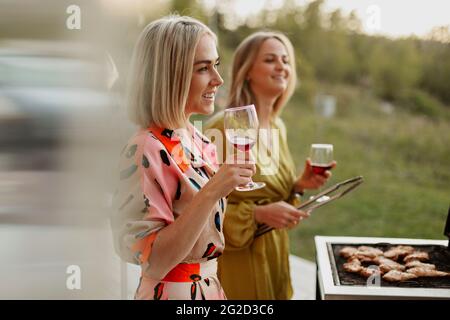 Amici femminili che tengono bicchieri di vino e carne alla griglia Foto Stock