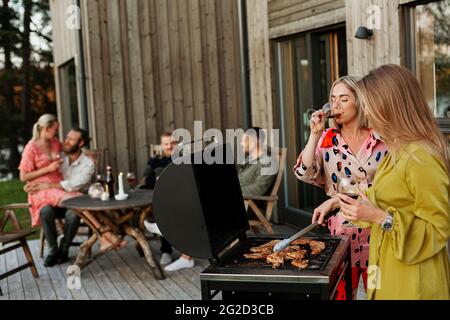 Amici che hanno barbecue e bere vino sul patio Foto Stock