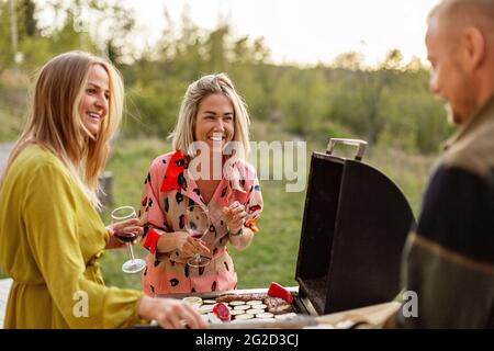 Amici preparare il cibo al barbecue e bere vino Foto Stock