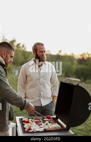 Amici maschili che preparano il cibo al barbecue Foto Stock