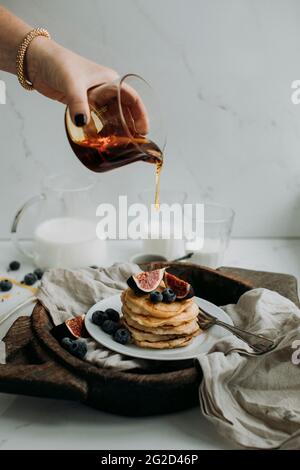 Donna che versa il miele sui pancake con fichi e mirtilli Foto Stock