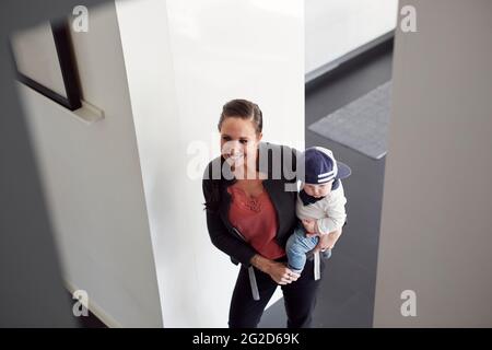 Donna sorridente che porta il figlio del bambino Foto Stock