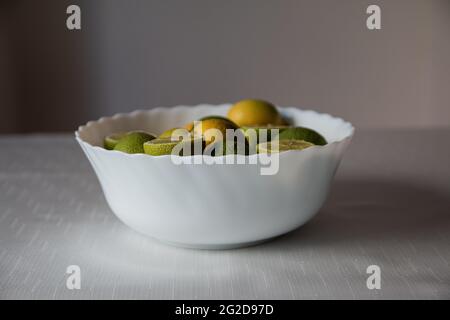 Lime verdi e limoni gialli all'interno della ciotola bianca, limone intero e affettato, agrumi Foto Stock