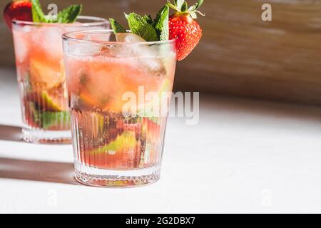 Rinfrescante cocktail estivo di caipirinha con fragole e menta fresca in bicchieri, luce dura con ombre Foto Stock