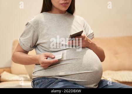 Donna incinta a casa con il telefono è seduto con il carrello di credito, concetto: Shopping online. Foto di alta qualità Foto Stock