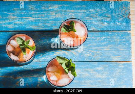 Bevande ghiacciate fatte in casa al succo di limone con fragole fresche e menta, limonata in bicchieri su rustico tavolo di legno blu Foto Stock