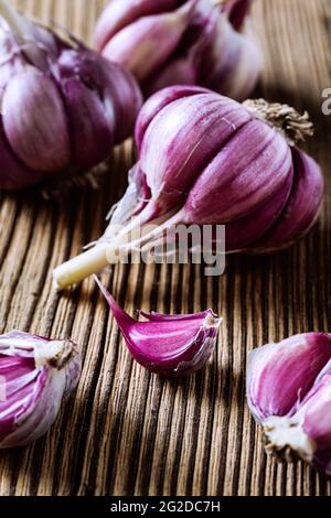 Aglio viola crudo su tavola di legno. Stile rustico, primo piano, messa a fuoco selettiva Foto Stock