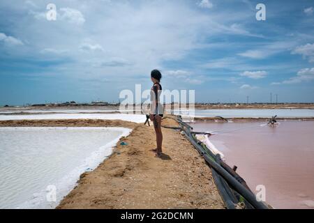 Manaure, la Guajira, Colombia - Maggio 29 2021: Giovane donna in piedi nel mezzo dei box acque del cielo rosa e blu nella più importante SA marittima Foto Stock
