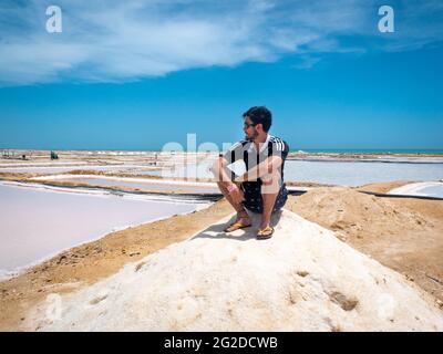Manaure, la Guajira, Colombia - 29 2021 maggio: Giovane latino seduto in una montagna di sale nelle più importanti stecche di sale marittime del Paese Foto Stock