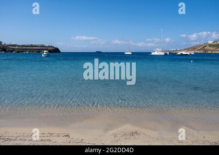 Isola di Mykonos, Cicladi. Grecia. Ornos spiaggia sabbiosa, concetto di vacanza estiva. Barche a vela e yacht ormeggiati in mare aperto, cielo blu chiaro sfondo. Vela Foto Stock