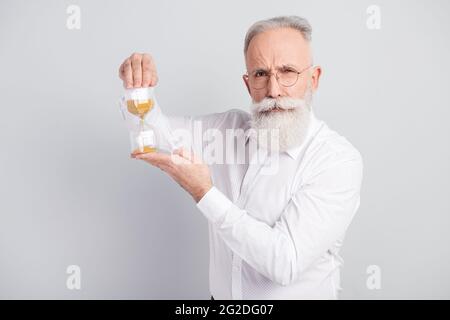 Foto di affascinante grave grave grave uomo tenere mani mostra clessidra sabbia isolato su sfondo grigio Foto Stock
