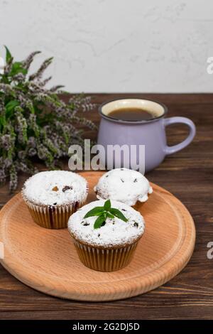 Cupcakes con ribes nero su sfondo di fiori e foglie di menta, su una tavola rotonda su sfondo di legno. Foto Stock