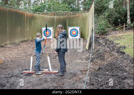 Un bambino piccolo ha un andare a tiro con l'arco di fronte a un bersaglio. Foto Stock