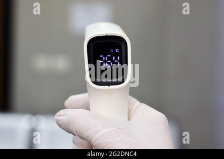 Termometro digitale per fronte a infrarossi senza contatto tenuto da un personale medico che controlla la temperatura corporea per i sintomi del virus Foto Stock