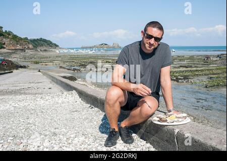 Una persona che prova le ostriche fresche dai letti di ostriche vicino al mare nel villaggio francese di Cancale in Bretagna sulla costa settentrionale della Francia. Foto Stock