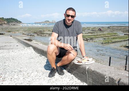 Una persona che prova le ostriche fresche dai letti di ostriche vicino al mare nel villaggio francese di Cancale in Bretagna sulla costa settentrionale della Francia. Foto Stock