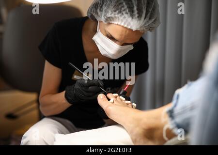 Pedicure master in maschere e guanti vernici unghie Foto Stock