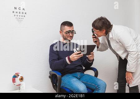 Un optometristo che conduce un esame dell'occhio su un paziente all'ottico per valutare la sua vista. Foto Stock