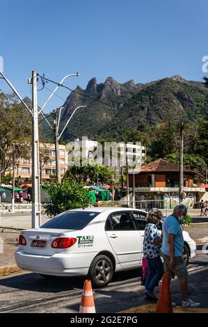 Un taxi bianco che passa per le strade di piazza Higino da Silveira con vista parziale delle tende dell'Alto Fiera, degli edifici e di una grande scarpata di montagna sul retro. Foto Stock