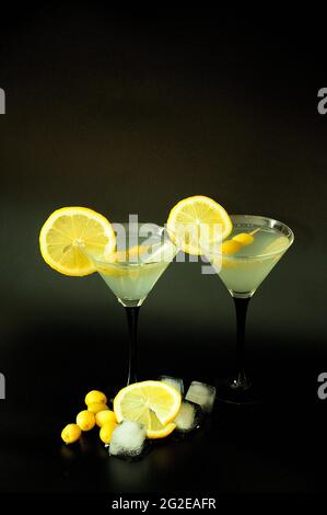 Due bicchieri di vermouth bianco con fette di limone e olive su fondo nero con ghiaccio. Posizionamento verticale. Foto Stock