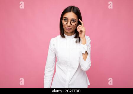 Foto di bella donna giovane e premurosa bruna che indossa abiti casual e occhiali ottici eleganti isolati su sfondo colorato aspetto Foto Stock