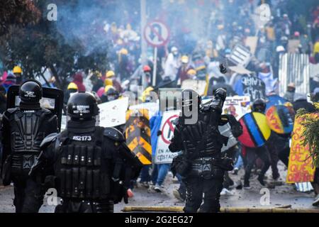 Un ufficiale della polizia in rivolta (ESMAD) della Colombia lancia un gas di trar e una granata di acrobazie ai dimostranti durante gli scontri, mentre le manifestazioni si intensificavano per disordini e scontri tra dimostranti e la polizia in rivolta della Colombia admisero dimostrazioni anti-governative contro il presidente della Colombia Ivan Duque, la brutalità e le disuguaglianze della polizia a Pato, Colombia, il 9 giugno 2021. Foto Stock