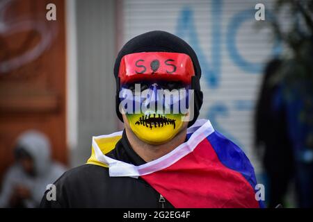 Un dimostratore indossa una maschera con i colori della bandiera nazionale colombiana e l'acronimo 'S.O.S' mentre le manifestazioni si intensificavano a disordini e scontri tra dimostranti e la polizia maledetta colombiana adnebulizza manifestazioni anti-governative contro il presidente della Colombia Ivan Duque, brutalità e disuguaglianze della polizia a Pato, Colombia, il 9 giugno 2021. Foto Stock