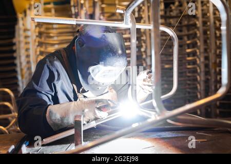 Saldatore che costrue acciaio in uno stabilimento di produzione. Artigiano del metallo che lavora nel suo ambiente di lavoro di ingegneria. Foto Stock