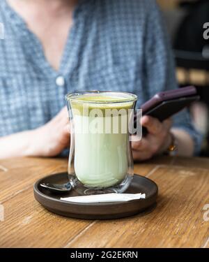 Tè verde matcha latte in una tazza di vetro su un tavolo di legno nel caffè. Drink perfetto per la colazione. Messa a fuoco selettiva. Foto Stock