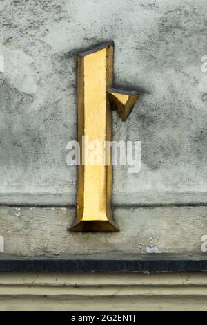 Lettera storica d'oro t con serifs su una parete grigia Foto Stock