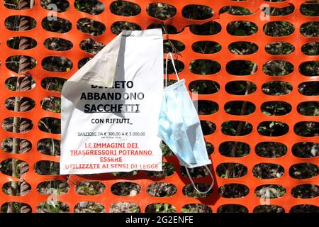 Somma Lombardo/Italia, giugno 2021: Cartello di avvertimento che vieta lo scarico dei rifiuti nel parco. L'abbandono della maschera chirurgica Covid-19 sulla recinzione di plastica rossa. Foto Stock