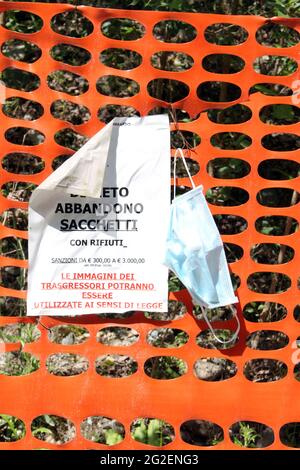 Somma Lombardo/Italia, giugno 2021: Cartello di avvertimento che vieta lo scarico dei rifiuti nel parco. L'abbandono della maschera chirurgica Covid-19 sulla recinzione di plastica rossa. Foto Stock