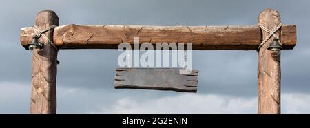 Cartello di legno vuoto sospeso da pali di legno. Cartello in legno vuoto con copyspace pronto per il tuo messaggio di testo, appeso sul palo a lato della campagna Foto Stock