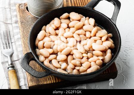 Set di fagioli bianchi in scatola, in padella di ghisa, su una superficie di pietra bianca Foto Stock