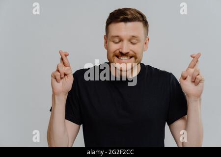 Giovane uomo credente che tiene le dita incrociate e sperando per la fortuna Foto Stock