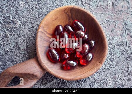 Capsule rosse di gel morbido di olio di krill su un cucchiaio, vista dall'alto. Integratore nutrizionale sano. Foto Stock