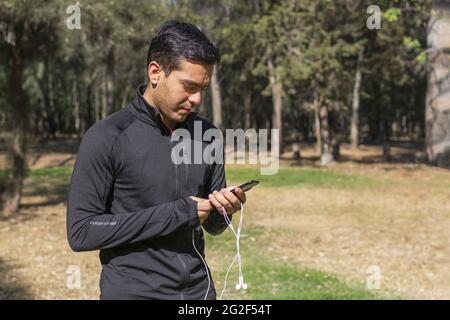 Giovane latino che usa il suo cellulare mentre corre attraverso la foresta mentre ascolta la musica. Foto Stock