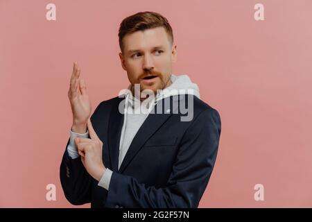 Uomo preoccupato che controlla la frequenza del polso mentre si trova contro la parete rosa in studio Foto Stock