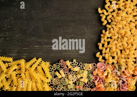 Diversi tipi di pasta cruda si trovano su un tavolo di legno scuro intorno al perimetro della foto Foto Stock