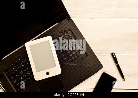 Un computer portatile, un eBook, una penna e un telefono cellulare si trovano su un tavolo di legno dai colori chiari. Sulla destra è presente un punto in cui inserire il testo Foto Stock
