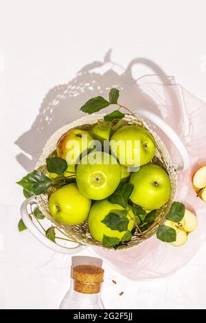 Composizione verticale con mele verdi in sacchetto di vimini e bottiglia con succo su fondo bianco. Concetto di mercato locale e frutti di fattoria Foto Stock