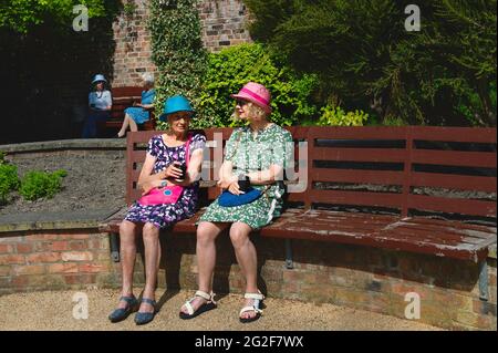 Due donne vestite con abiti colorati e cappelli godono di una bella mattina di primavera nei giardini pubblici di Beverley, Yorkshire, Regno Unito. Foto Stock