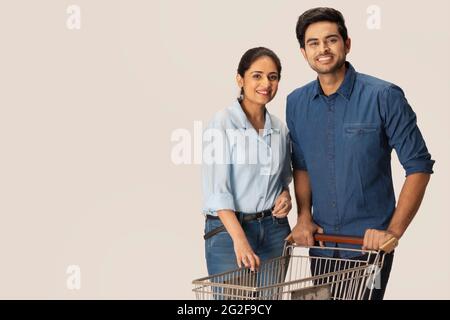UNA COPPIA FELICE IN POSA DAVANTI ALLA MACCHINA FOTOGRAFICA MENTRE TIENE IL CARRELLO DELLA SPESA Foto Stock
