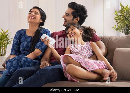 UNA FAMIGLIA ALLEGRA CHE RIDE FELICE INSIEME MENTRE SI SIEDE COMODAMENTE A CASA Foto Stock