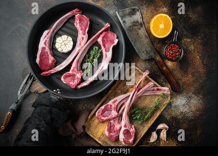 Costolette fresche di agnello crude, con ingredienti arancia carota, erbe, su padella di ghisa, su vecchio sfondo rustico scuro, vista dall'alto piatto Foto Stock